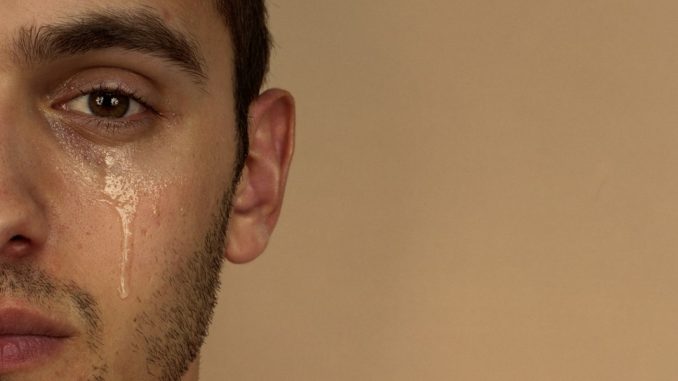Young man with tear rolling down cheek, portrait, close-up